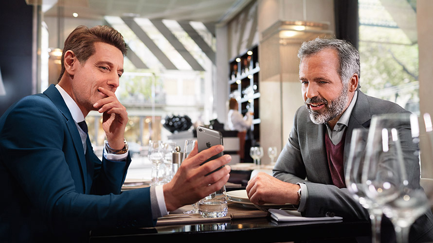 Dine favoritsteder To mænd i en restaurant bruger funktionen "Dine favoritsteder" på smartphone