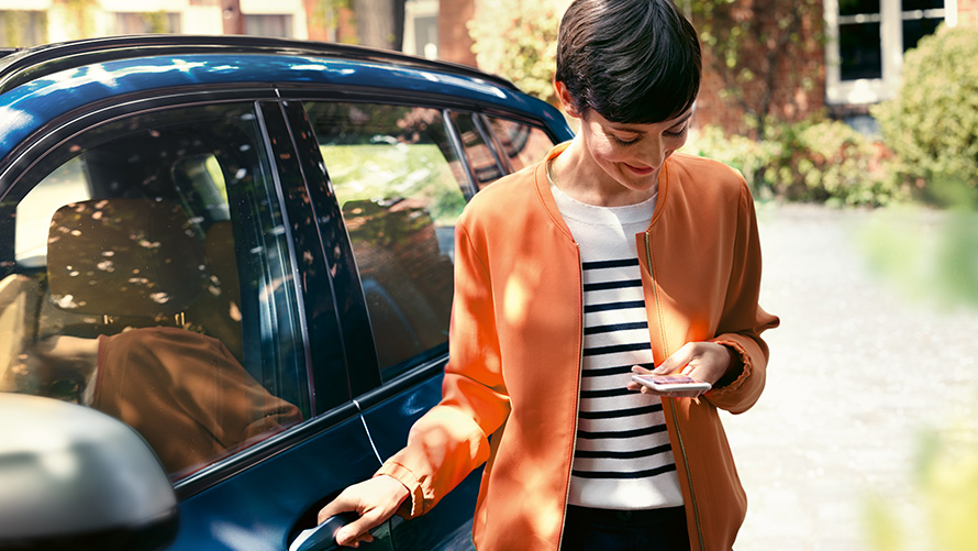BMW Teleservices En kvinde med en smartphone står ved døren til sin BMW