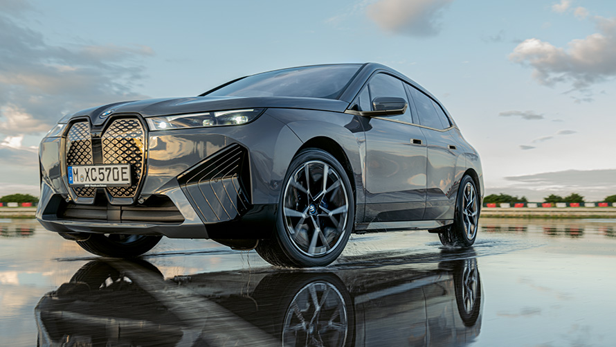 BMW Fælge, BMW iX (i20) set forfra let drejet på en våd vej BMW Fælge, BMW iX (i20) set forfra let drejet på en våd vej