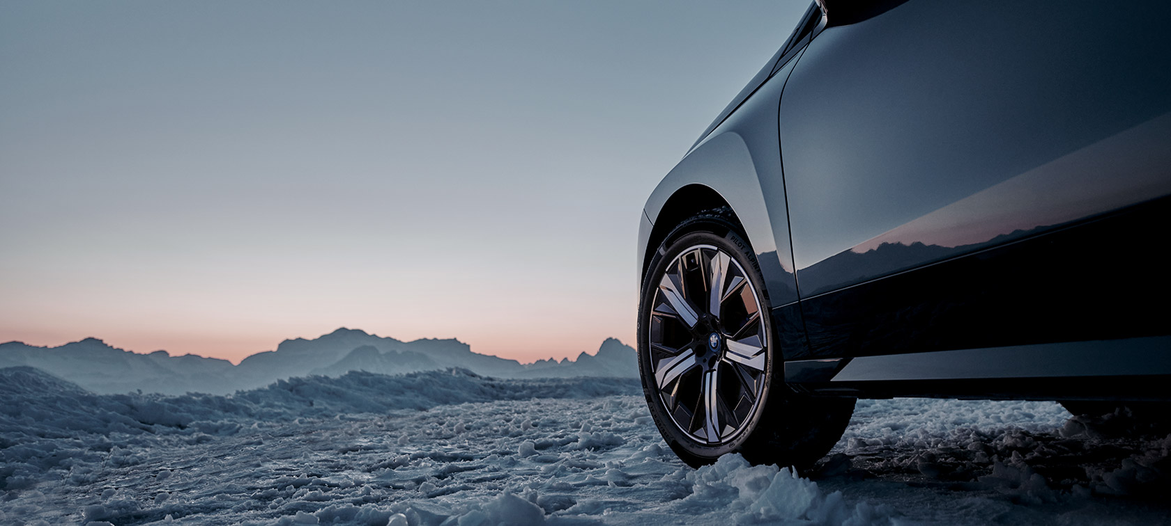 Originale BMW fælge på BMW iX (I20) i sne med bjerge i baggrunden Originale BMW fælge på BMW iX (I20) i sne med bjerge i baggrunden