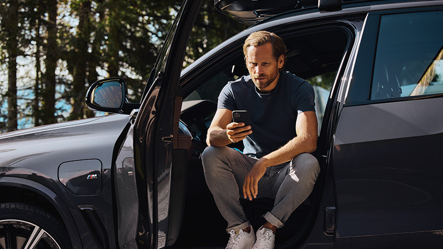 En mand sidder i en BMW og kigger på sin smartphone BMW forårs- og sommertilbehør En mand sidder i en BMW og kigger på sin smartphone