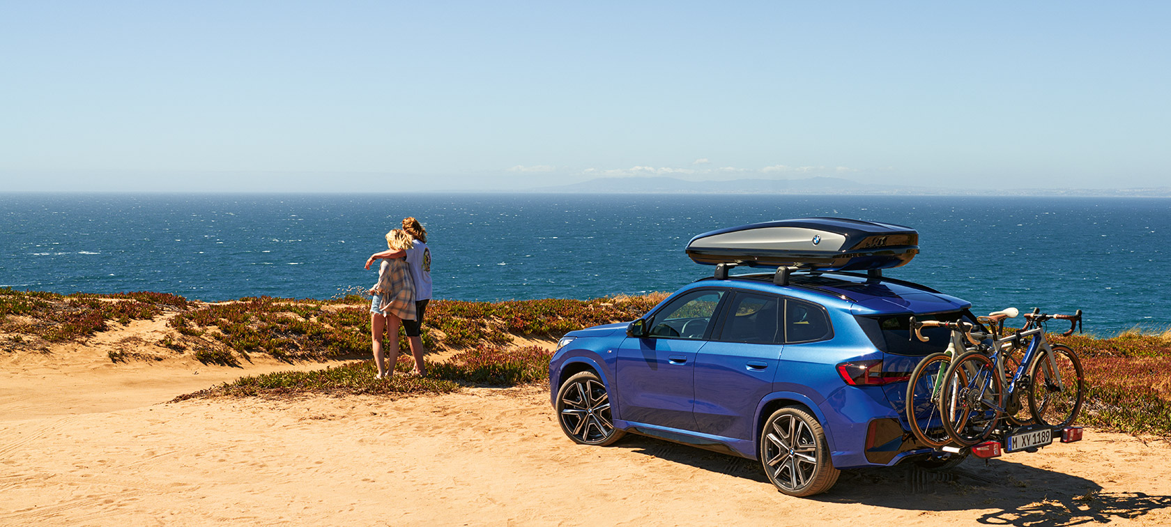 BMW Originaltilbehør til forår og sommer BMW X1 U11 BMW Originaltilbehør til forår og sommer BMW X1 U11 holdende på en strand med 2 personer
