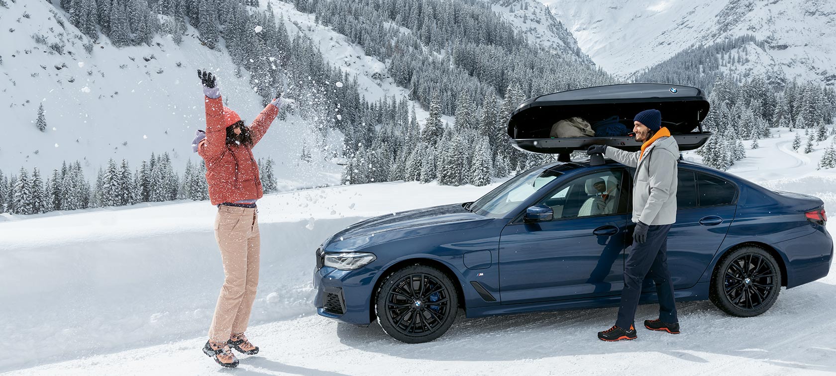 BMW Originaltilbehør og BMW Service til efterår og vinter En kvinde og en mand griner på kælkeudstyr i sneen
