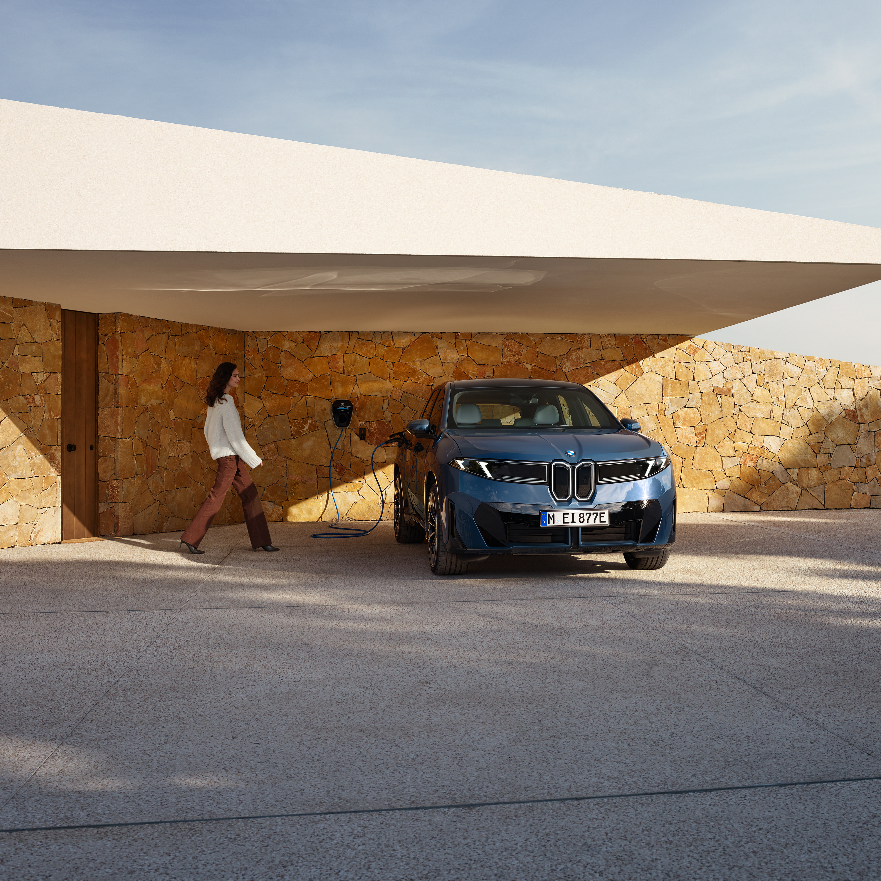 En kvinde går mod en BMW iX3, som er tilkoblet en wallbox